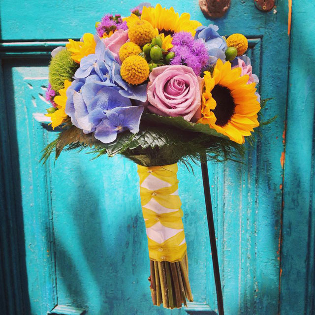 Ramo de novia divertido y colorido compuesto con girasoles, hortensia azul, rosas y crasperia.