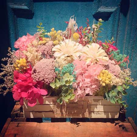 Caja de madera blanca decorada con flor preservada y seca en tonos blancos, fucsias, rosas y amarillos. Es un centro de tamaño grande, ideal para colocar en una mesa. Los materiales utilizado están tratados