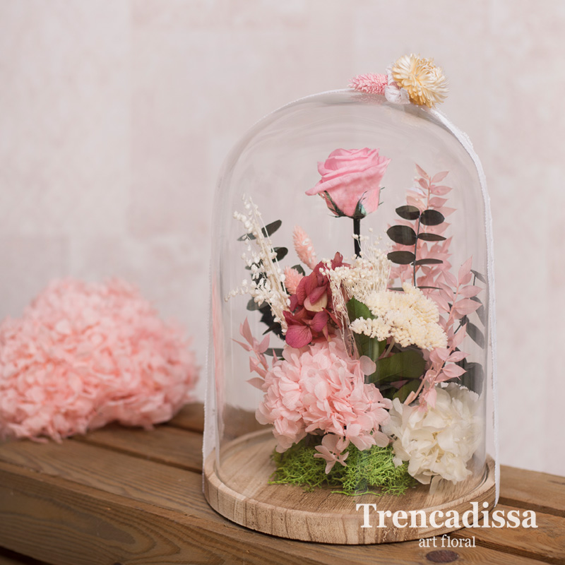 Cúpula o campana de vidrio con flor seca y preservada en tonos rosados