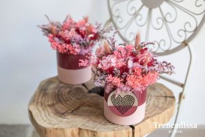Recipiente de cerámica en tonos rosa y rojo decorado con hortensia preservada y flor seca con corazón decorativo.