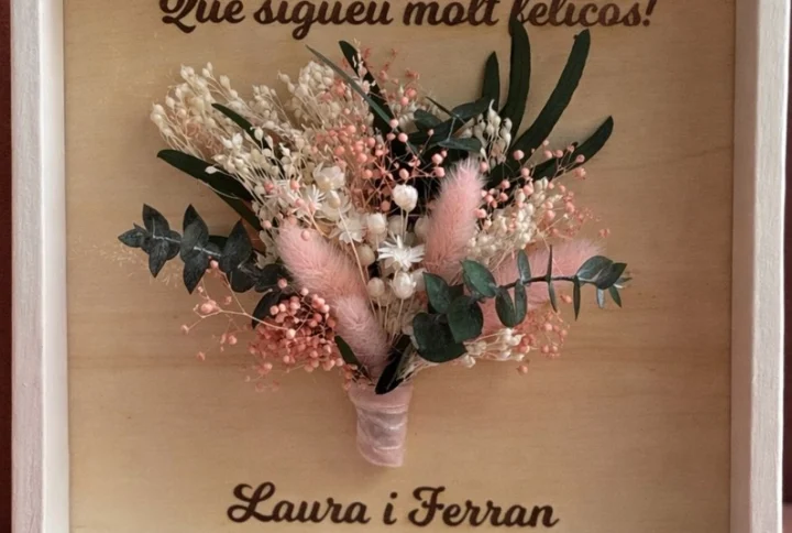 Marco personalizado de madera con flores secas y preservadas Creamos un marco único y artesanal, elaborado en madera y decorado con flores secas y preservadas en los mismos tonos que el ramo de la novia. Podrás personalizarlo con los nombres de los novios, la fecha especial y la frase que tú elijas para convertirlo en un recuerdo eterno. Para elegir los textos y los colores del ramillete, así como concretar cualquier detalle de tu diseño, ponte en contacto con nosotros. Estaremos encantados de ayudarte a crear una pieza tan especial como vuestro día.