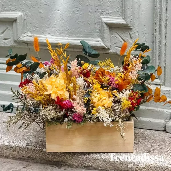Caja de madera de estilo vintage con flor seca y preservada, en tonos amarillo, naranjas y verde.