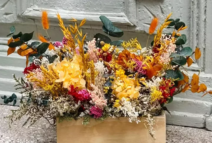 Caja de madera de estilo vintage con flor seca y preservada, en tonos amarillo, naranjas y verde.