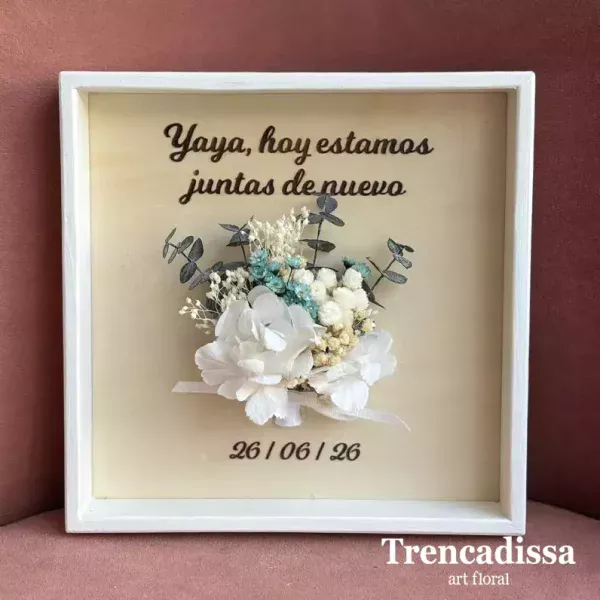 Marco personalizado de madera con flores secas y preservadas Creamos un marco único y artesanal, elaborado en madera y decorado con flores secas y preservadas en los mismos tonos que el ramo de la novia. Podrás personalizarlo con los nombres de los novios, la fecha especial y la frase que tú elijas para convertirlo en un recuerdo eterno. Para elegir los textos y los colores del ramillete, así como concretar cualquier detalle de tu diseño, ponte en contacto con nosotros. Estaremos encantados de ayudarte a crear una pieza tan especial como vuestro día.